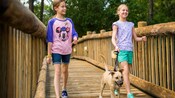 Two girls walk a small dog on a leash across a wooden bridge