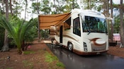 An RV with awning parked on a cement pad in a campsite after a rain
