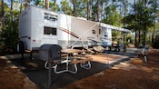 Campsite with an RV parked on its concrete pad that includes a charcoal barbecue grill and picnic table