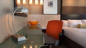 Uma mesa com tampo de vidro e cadeira de escritório ao lado de uma cama no Disney's Contemporary Resort