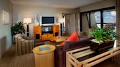 Área de estar con TV de pantalla plana, consola multimedia, butacas, un sofá y cómoda con una maceta