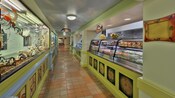 Un couloir avec des terrariums et une vitrine remplie de nourriture à emporter avec une enseigne indiquant « Picabu Greens »