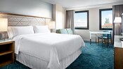 Une chambre avec un lit, des oreillers, une causeuse, une table, une chaise, des rideaux et une vue de l’hôtel Walt Disney World Swan Hotel à proximité