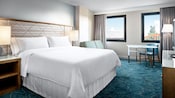 Una habitación con cama, almohadas, un sofá de dos plazas, una mesa, una silla, cortinas y vista al hotel aledaño Walt Disney World Swan Hotel