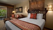Una cama con una cabecera ásperamente tallada, 2 lámparas de pared, adorno de pared, sofá, mesa baja y balcón