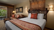 Un lit avec une tête de lit grossièrement sculptée, 2 appliques murales, décoration murale, canapé , table basse et balcon