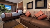 Una mesa ratona, un sofá, un cuadro enmarcado, 2 lámparas de pared, una cama con cabecera de madera, un tapiz y un balcón