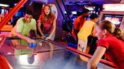 2 teens playing a game of air hockey against each other in a Disney hotel arcade