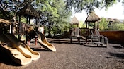 Une aire de jeux en gravier avec des glissades et des plateformes sous un toit en chaume au Disney’s Animal Kingdom Villas – Kidani Village