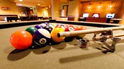 Close-up of a tan pool table with balls racked up next to a pool stick and chalk