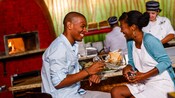 A couple laughs as they drink near food and a kitchen staff member