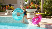 2 girls with inner tubes jumping into a pool