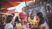 Una familia come en la mesa mientras una camarera sostiene una bandeja de comida