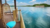 A hanging wicker chair on the terrace of an overwater bungalow looks out to the water and Resort