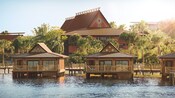 Tres bungalows junto al agua con palmeras en el fondo