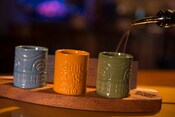 Liquer is poured into 3 cups with the words Trader Sam's Grog Grotto emblazoned on a cup