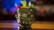 A drink in a mug fashioned to resemble a smiling shrunken head