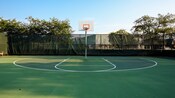 A basketball hoop in a large fenced green court