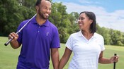 Um homem e uma mulher caminham em um campo de golfe, cada um segurando um taco