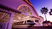 A Monorail glides out of a station that’s lit in a purple hue