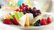 A plate with various types of cheeses paired with strawberries, blueberries, melon slices, grapes and raspberries