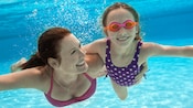 Une mère nage sous l’eau avec sa fille portant des lunettes de natation