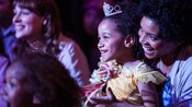 A smiling young girl wears a Disney Princess costume and sits on her mother's lap