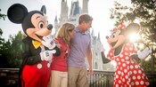 A middle-aged couple in front of Cinderella’s Castle chat with Mickey Mouse and Minnie Mouse