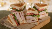 A turkey club sandwich, divided into 4 sections with each section held together by a toothpick, is served on a wooden board