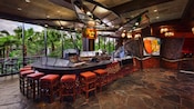 Curved sushi-bar with stools, next to floor-to-ceiling windows with a view of palm trees