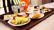 Room service tray containing 2 cups of coffee, croissants, a pitcher of juice, glasses of ice and a plate of fresh-cut fruit