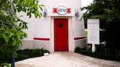 Edificio blanco con puerta roja y un letrero que dice 