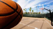 Primer plano en perspectiva de un balón frente a una cancha de baloncesto.