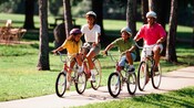 Une famille de 4 membres portant des casques roule à vélo sur un chemin en béton