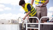 Un huésped joven con un chaleco salvavidas saca una lubina de boca grande recién pescada del agua mientras su padre lo observa