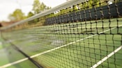 Close-up of a tennis net and its court in the background