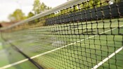 Close-up of a tennis net and its court in the background