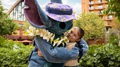 A girl getting a hug from Stitch surrounded by trees near a Disney Resort hotel