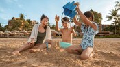 A mother and her 2 children building a sandcastle on the beach at Aulani, A Disney Resort & Spa