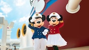 El Capitán Mickey Mouse y la Capitana Minnie Mouse saludan con la mano junto a las chimeneas de un barco de Disney