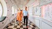 Una pareja caminando por la entrada de Animator’s Palate, llena de bocetos de Personajes de Disney