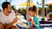 A man and his daughter eating ice cream cones on a beach