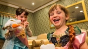 Dos niñas vestidas como Anna y Elsa se ríen mientras juegan con muñecas de Olaf