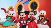 Mickey Mouse, Minnie Mouse, Donald Duck and Daisy Duck dressed in their holiday attire while posing together on a Disney cruise ship