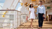 A smiling couple holding hands as they take a stroll on the deck of the Disney Wish ship