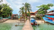 A wooden dock leading to a small waterfront village in Panama with boats, palm trees and tropical buildings along the shore