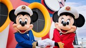 Captains Mickey Mouse and Minnie Mouse holding hands aboard a Disney cruise ship 