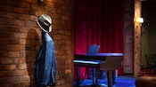 A small stage with a piano and a coatrack with a suit jacket and fedora in the Soul Cat Lounge aboard the Disney Magic