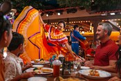 Cinco Huéspedes cenando mientras músicos y bailarines actúan en Plaza de Coco a bordo del Disney Treasure