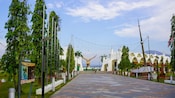 A paved promenade lined with trees, flag poles and string lights leading toward Eagle Square